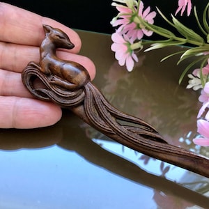 Può includere: Un fermacapelli in legno fatto a mano con un motivo a volpe intagliata. L'accessorio per capelli è realizzato in legno marrone scuro e presenta dettagli intricati. La volpe è raffigurata in una posa rilassata, aggiungendo un tocco di eleganza ispirata alla natura.