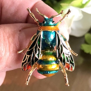 May include: A gold-toned bee brooch with black and green wings, a blue and yellow body, and red accents.