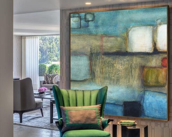 May include: A green velvet armchair with a gray pillow sits in front of a large abstract painting with blue, brown, and white colors. The painting is framed in a dark wood frame. A black side table with a book on top sits next to the chair.