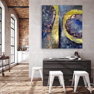 May include: Abstract painting with blue, gold, and copper tones. The painting features a large, circular shape with a smaller, circular shape inside. The painting is hanging on a wall in a modern kitchen.