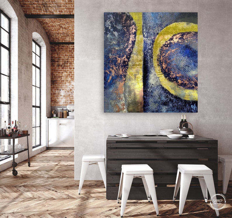 May include: Abstract painting with blue, gold, and copper tones. The painting features a large, circular shape with a smaller, circular shape inside. The painting is hanging on a wall in a modern kitchen.