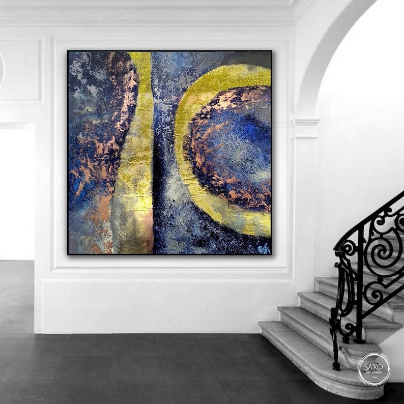 May include: Abstract painting with gold, blue, and pink colors. The painting features a large circle with a smaller circle inside. The background is a textured blue.