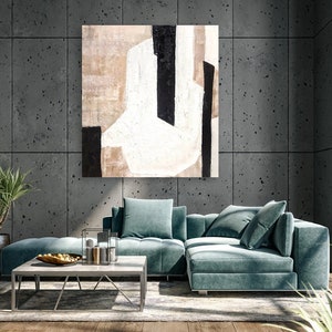 May include: A teal sectional sofa with a large abstract painting above it. The painting is in shades of white, black, and brown. The sofa is in a modern living room with a concrete wall and a large window.
