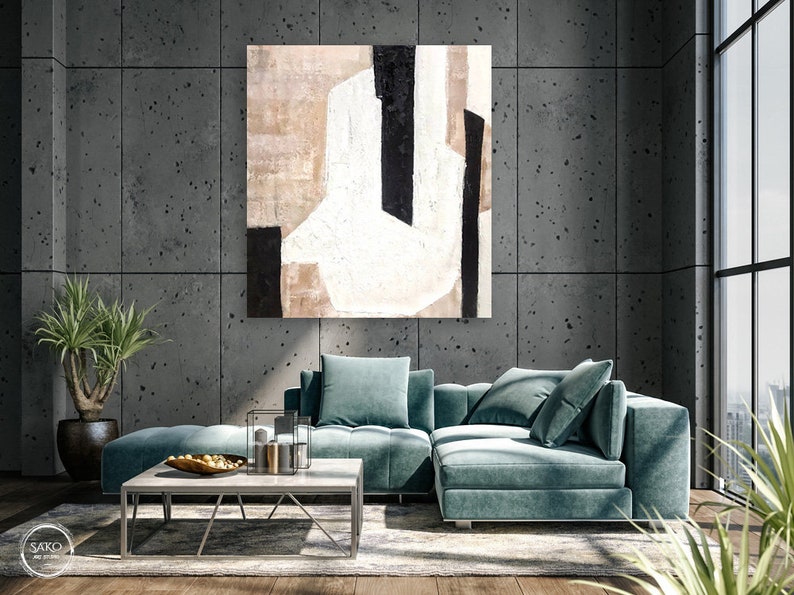 May include: A teal sectional sofa with a large abstract painting above it. The painting is in shades of white, black, and brown. The sofa is in a modern living room with a concrete wall and a large window.