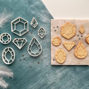 Könnte beinhalten: Ein Set mit 10 Ausstechern in Form verschiedener Edelsteine. Die Ausstecher sind aus weißem Kunststoff und auf einer weißen Oberfläche angeordnet. Die Ausstecher sind in zwei Reihen angeordnet, wobei die obere Reihe fünf Ausstecher und die untere Reihe fünf Ausstecher enthält.