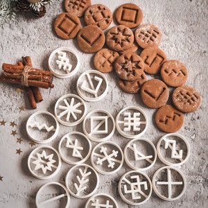 Könnte beinhalten: Ein Set mit 18 weißen Ausstechern mit verschiedenen geometrischen und Schneeflocken-Designs. Die Ausstecher sind in einem Kreis auf einem grauen Hintergrund angeordnet. Es gibt auch mehrere braune Lebkuchen mit ähnlichen Designs.