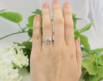 May include: A silver-toned ring featuring a single, large, round-cut clear gemstone set in a four-prong setting. The band is smooth and polished, showcasing a classic design that highlights the brilliance of the central stone.