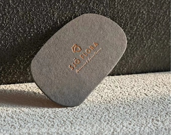May include: A grey, oval-shaped business card with the text "Sjö Flora" in gold lettering.
