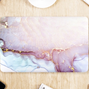 May include: Laptop skin with an abstract design. The design features flowing patterns in shades of pink, purple, and blue, accented with gold veins. The laptop skin is rectangular and sits on a wooden surface.