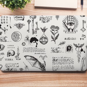 Op de afbeelding: Een laptop-huid met een zwart-wit ontwerp met verschillende illustraties, waaronder sleutels, een schedel, een vleermuis, een hand met een oog en tekst. De tekst bevat de woorden "Queen", "Terra", "Lapidem Occultum" en "Alchemy".