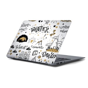 May include: A white laptop with a gold and black doodle design. The design includes stars, hearts, mountains, clouds, and the words "WONDER", "TRAVEL", "WANDER", and "To live it".