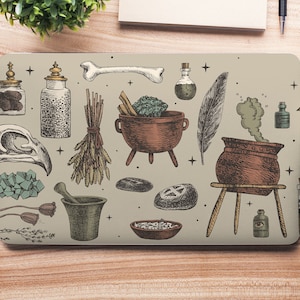 Op de afbeelding: Een laptop skin met een vintage illustratie van verschillende heksenvoorwerpen, waaronder een ketel, kruiden, botten en flesjes met toverdrank. Het ontwerp is in tinten bruin, groen en wit op een beige achtergrond.