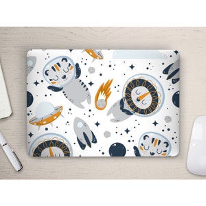 Könnte beinhalten: Eine weiße Laptop-Haut mit einem sich wiederholenden Muster aus einem Tiger und einem Löwen, die Astronautenhelme tragen, einer Rakete, einem UFO und Sternen. Der Hintergrund ist weiß mit blauen und orangefarbenen Akzenten.