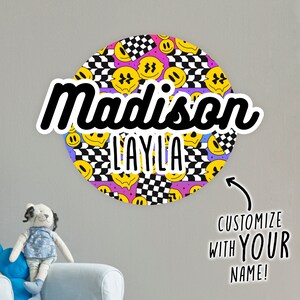 May include: A round sticker with a black and white checkered pattern, yellow smiley faces, and the name "Madison Layla" in black text. The sticker is customizable with your name.