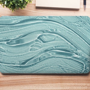 May include: A laptop computer with a teal blue abstract design on the lid. The laptop is on a wooden desk with other office supplies.
