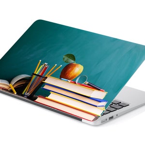 Può includere: Un laptop con un design di lavagna verde che presenta una pila di libri, una lente d'ingrandimento, matite e una mela rossa con una foglia verde.