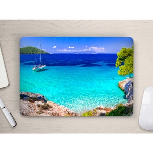 May include: A white sailboat at anchor in a turquoise blue lagoon with a small island in the background. The water is crystal clear and the sky is a bright blue.