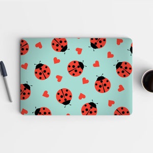 Könnte beinhalten: Eine Laptop-Haut mit einem sich wiederholenden Muster aus roten Marienkäfern und weißen Herzen auf hellblauem Hintergrund.