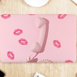 May include: A pink laptop computer with a pink rotary phone on top. The laptop has a pink background with red lipstick kiss marks.