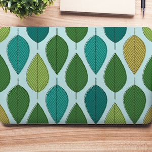 Könnte beinhalten: Ein Laptop mit einem blauen und grünen Blatt-Muster auf der Abdeckung. Die Blätter sind schwarz umrandet und haben eine strukturierte Optik.