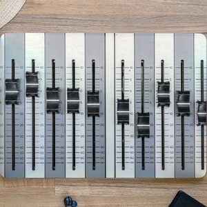 May include: A silver mixing board with multiple faders, each with a black knob. The faders are labeled with numbers from 0 to 60.