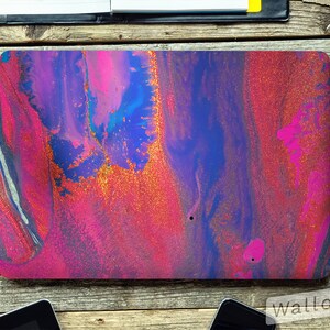 May include: A laptop skin with an abstract design featuring pink, blue, and gold colors. The design resembles swirling liquid with a glittery texture.