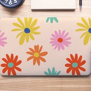 Puede incluir: Un ordenador portátil con un diseño floral. El diseño presenta flores amarillas, naranjas, rosas y azules sobre un fondo rosa claro.