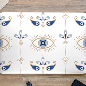 May include: A white laptop skin with a repeating pattern of blue and gold evil eyes. The evil eyes are stylized with a teardrop shape and a circle in the center. The background is white with a subtle texture.