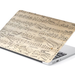 May include: A laptop computer with a cream-colored case featuring a vintage music sheet design. The sheet music is printed in black ink and includes musical notes, clefs, and a handwritten inscription.