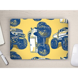 Könnte beinhalten: Gelbe Laptop-Matte mit einem sich wiederholenden Muster aus blauen und weißen Monstertrucks. Die Trucks sind mit großen Reifen und detaillierten Designs illustriert. Die Matte ist rechteckig und liegt auf einer hellen Holzoberfläche.