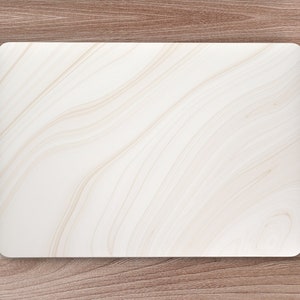 以下が含まれることがあります： 蓋に大理石のようなデザインが施された白いラップトップ。ラップトップは、左側にノートとペン、右側に白いワイヤレスマウスのある木製デスクの上に置かれています。