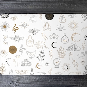 Op de afbeelding: Een witte achtergrond met een patroon van zwarte en gouden lijntekeningen van verschillende mystieke en occulte symbolen, waaronder manen, sterren, ogen, slangen, insecten, kristallen en handen.
