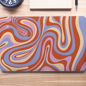 Puede incluir: Una piel para portátil con un patrón abstracto en espiral en tonos naranja, azul, morado y crema.