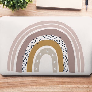 May include: A laptop computer with a rainbow design on the lid. The rainbow is made up of multiple shades of pink, brown, and yellow with black polka dots. The laptop is on a wooden surface.