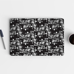 May include: Black laptop skin with a repeating white geometric pattern. The design features a series of interconnected shapes and lines. A pen and a cup of coffee are on the white surface.