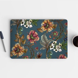 Op de afbeelding: Een laptop skin met een bloemenpatroon. Het ontwerp bevat verschillende bloemen in tinten rood, oranje, geel en wit op een donkerblauwe achtergrond.