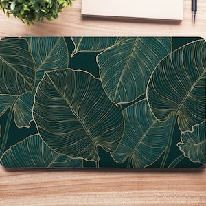 Puede incluir: Una funda para portátil con un diseño de hojas tropicales. Las hojas están delineadas en oro y sobre un fondo verde oscuro.