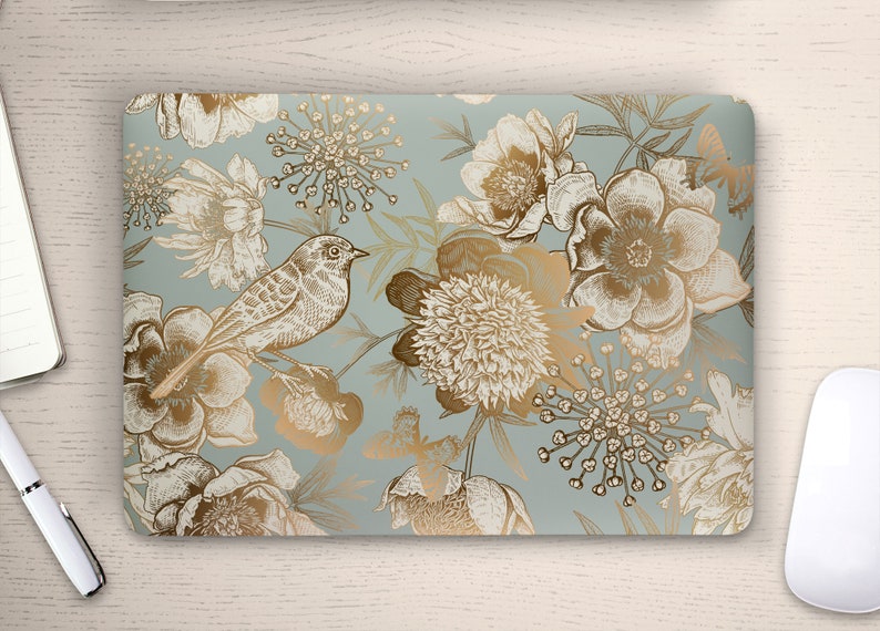 May include: A laptop skin with a floral pattern in gold and white on a light blue background. The design features birds, flowers, and leaves.