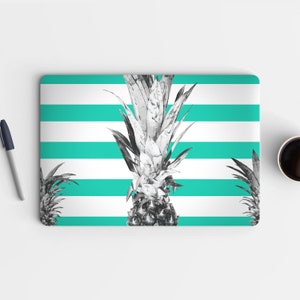 Op de afbeelding: Een laptop-huid met een witte en turquoise gestreepte achtergrond en een zwart-wit ananasontwerp.