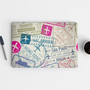 May include: A laptop skin with a vintage travel theme. The design features multiple passport stamps with various city names, dates, and arrival and departure stamps. The stamps are in shades of pink, blue, green, and brown.