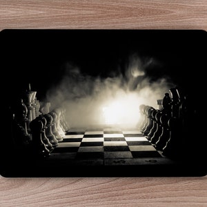 May include: A black and white chessboard with chess pieces arranged in a line on either side of the board. The board is lit from the center, creating a dramatic effect. The pieces are silhouetted against a dark background.