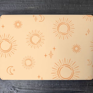 Puede incluir: Una funda para portátil con fondo melocotón y un patrón repetido de soles y estrellas naranjas.