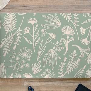 以下が含まれることがあります： 白い花の模様がついた緑色のノートパソコンのカバー。デザインは、様式化された花、葉、茎を特徴としています。