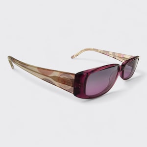 Puede incluir: Gafas de sol rectangulares con montura morada oscura y lentes degradadas moradas. Las patillas presentan un diseño estampado en tonos marrones, rosas y beige. El diseño general es de estilo retro.