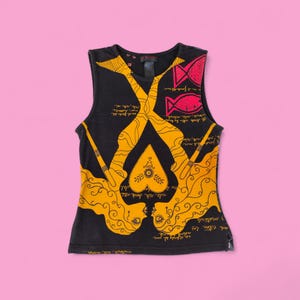 Op de afbeelding: Zwart mouwloos topje met een opvallend design. Het heeft twee gele gestileerde figuren die tegenover elkaar staan, met een hartvormig element in het midden. Rode vissen en tekst zijn ook aanwezig. De top is gemaakt van zacht materiaal.