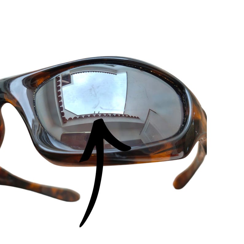 Puede incluir: Primer plano de gafas de sol con montura de carey. Las lentes oscuras reflejan un edificio y el cielo. La montura tiene un acabado brillante y un dise&ntilde;o cl&aacute;sico y deportivo. Las patillas de las gafas son visibles.
