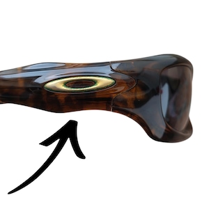 Puede incluir: Gafas de sol marrones y negras con un patr&oacute;n de carey. Las gafas de sol tienen un emblema dorado en el lateral. La montura es curvada y tiene un dise&ntilde;o elegante.