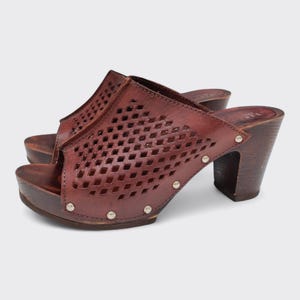 May include: A pair of brown leather clogs with a peep-toe design. The clogs feature a diamond-patterned cutout on the upper and are accented with silver studs. They have a wooden platform sole and a chunky wooden heel.