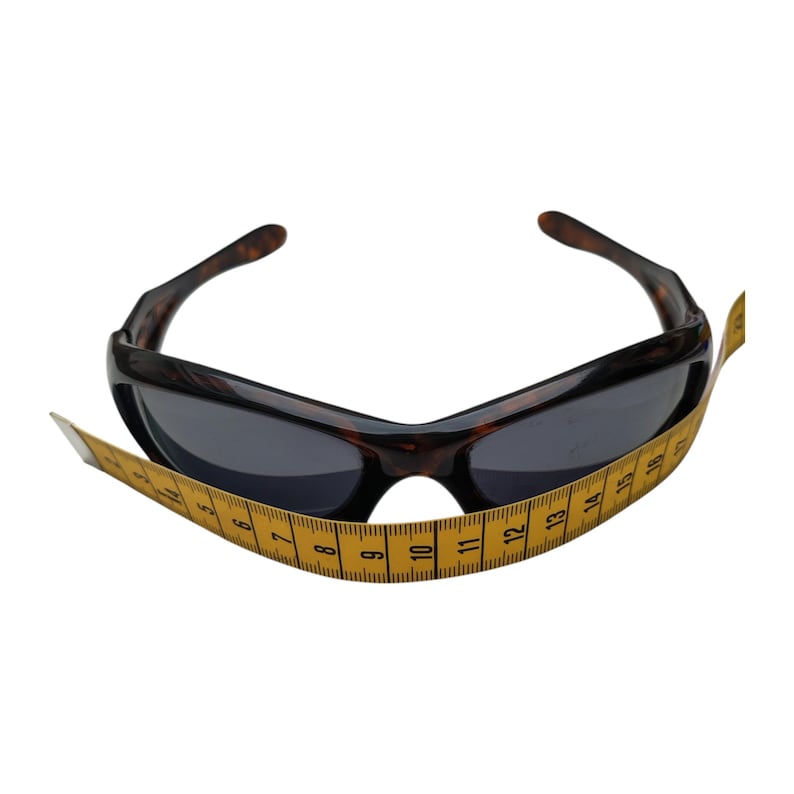 Puede incluir: Gafas de sol marrones oscuras con montura con estampado de carey y lentes oscuras. Una cinta m&eacute;trica amarilla est&aacute; envuelta alrededor de las gafas de sol. Estilo deportivo.