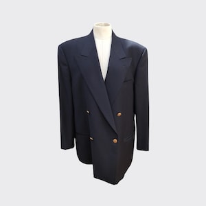 Puede incluir: Un blazer azul marino de doble botonadura con botones dorados. El blazer se exhibe en un maniquí con una camisa blanca debajo. El diseño del blazer es clásico y entallado.